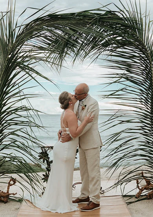 Gorm and bride's first kiss underneath a beatiful palmtree made arch