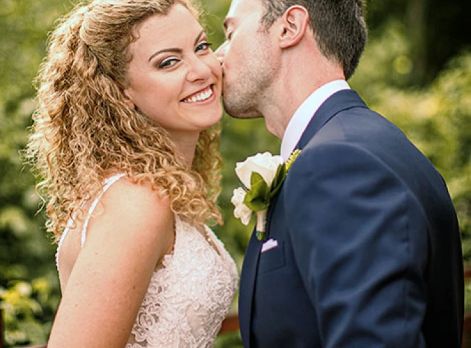 Bride smiles when groom kisses her chick