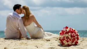 Couple kisses on the beach on the background as the bride's bouquet shows in foreground.