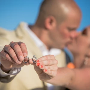 Bride and Groom showing their wedding bands while kissing on background.