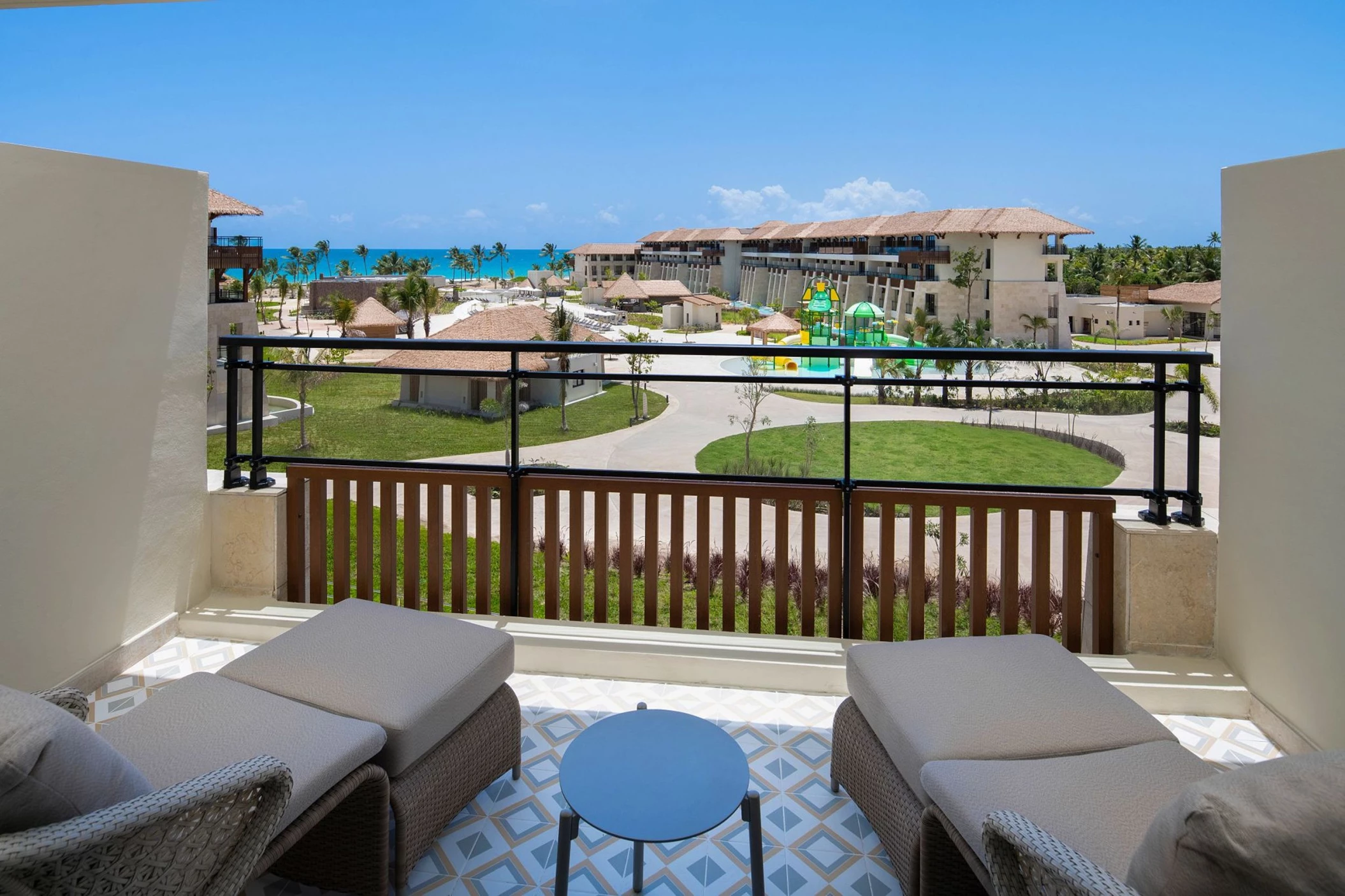 A balcony with lounge chairs offering a partial ocean view of the resort and its pools and water park.