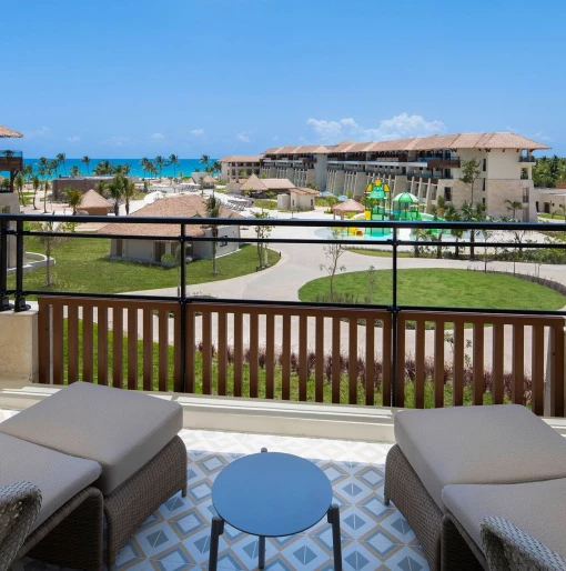 A balcony with lounge chairs offering a partial ocean view of the resort and its pools and water park.
