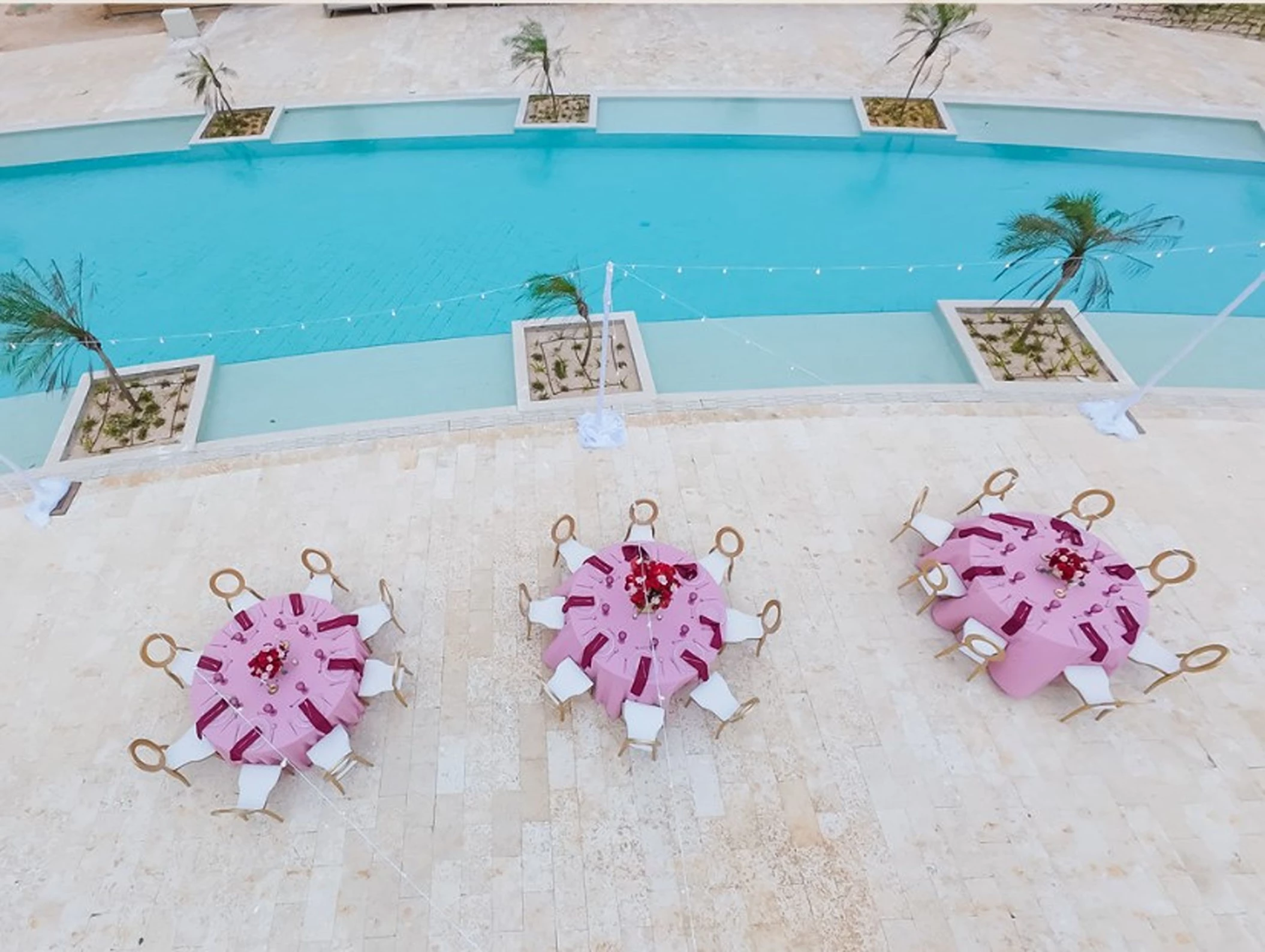 An outdoor terrace with three tables set for a dinner, overlooking a beautiful turquoise blue swimming pool.