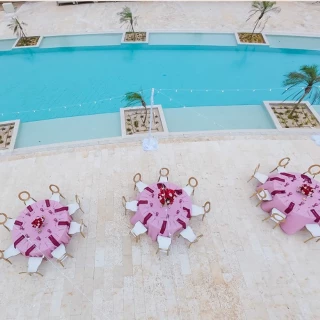An outdoor terrace with three tables set for a dinner, overlooking a beautiful turquoise blue swimming pool.
