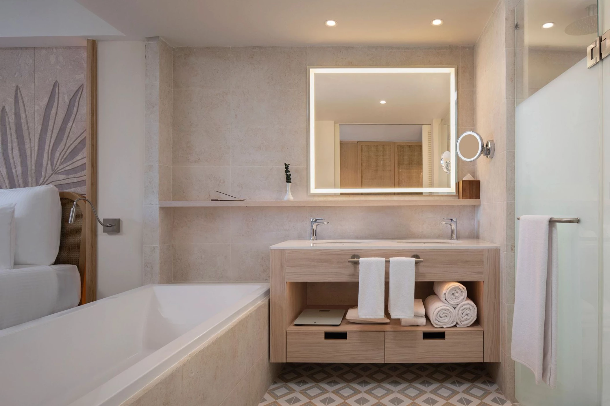 A bathroom with a double vanity, a large illuminated mirror, a bathtub, and a separate glass-enclosed shower.