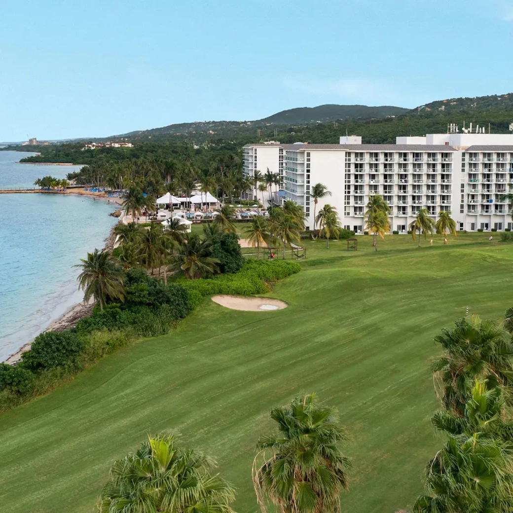 Aerial view of the Dreams Rose Hall Resort & Spa, showcasing the hotel buildings, ocean, and lush green golf course.