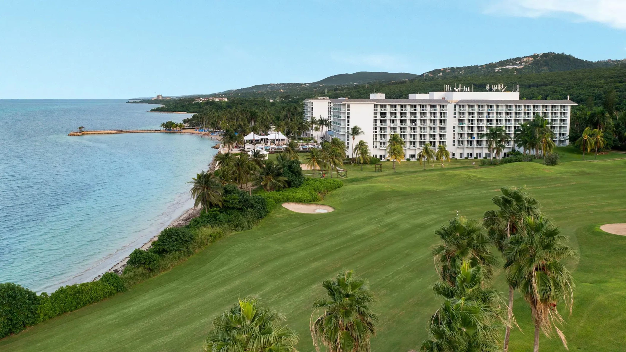 Aerial view of the Dreams Rose Hall Resort & Spa, showcasing the hotel buildings, ocean, and lush green golf course.