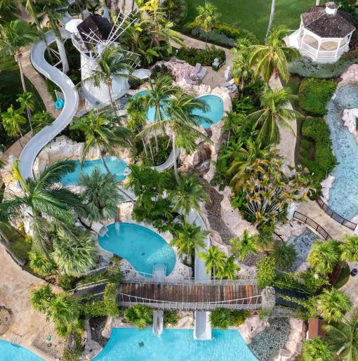 An aerial view of the resort's multi-level swimming pools, water slides, and palm-tree-filled grounds.