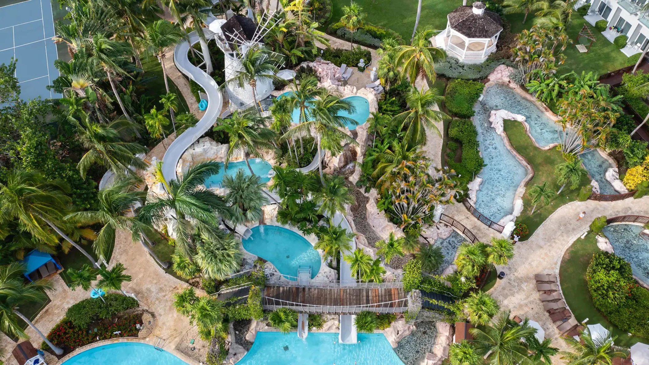An aerial view of the resort's multi-level swimming pools, water slides, and palm-tree-filled grounds.