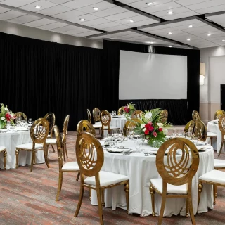 The beautifully set-up ballroom venue at the resort, featuring round tables, elegant gold chairs, and a screen.