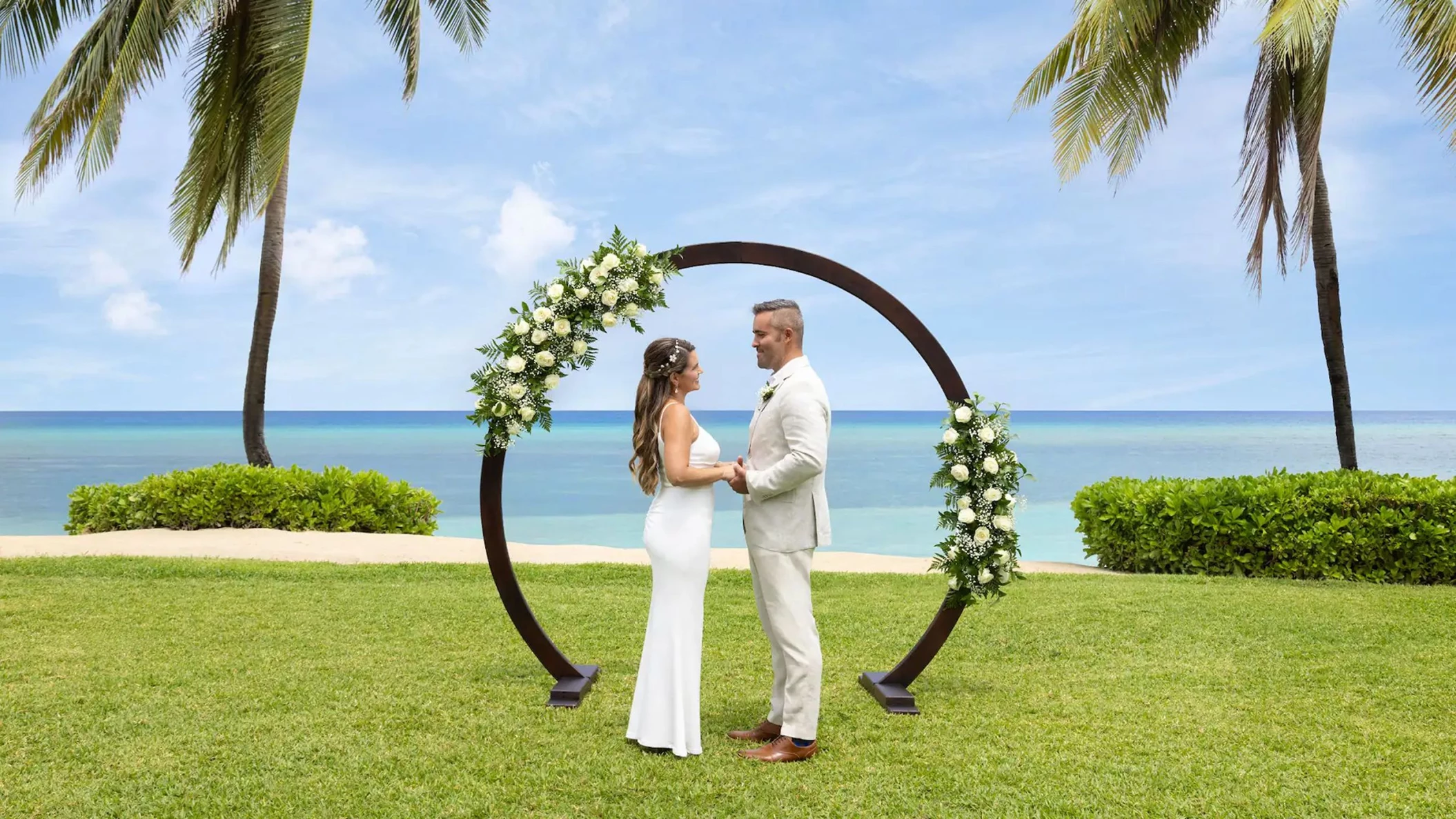 A bride and groom standing at the resort's West Lawn wedding venue with the ocean in the background.