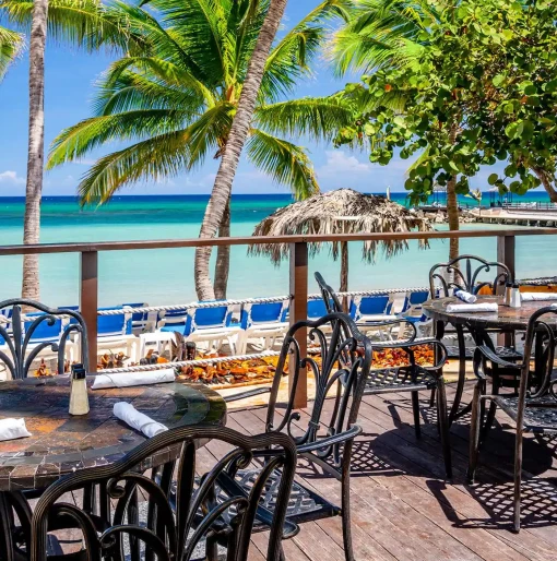 Outdoor seating at Mangoes Restaurant, with tables on a deck and a beautiful view of the beach and ocean.