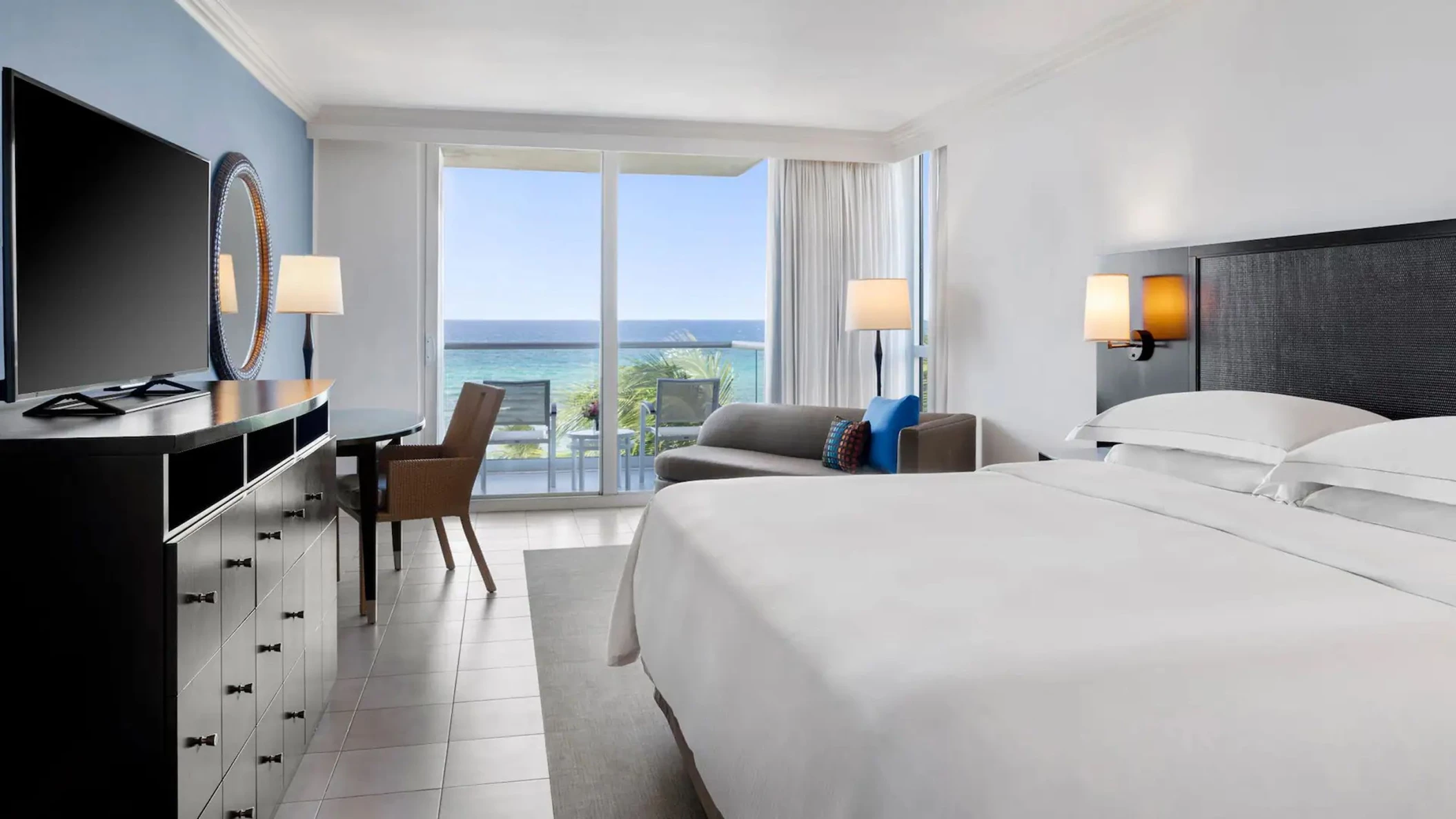 The elegant bedroom of an Oceanfront Royal Suite with a king-sized bed and a balcony overlooking the sea.