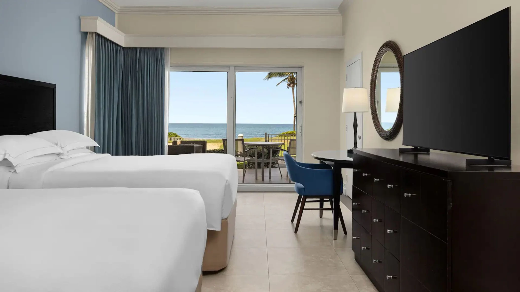 An Oceanfront Walkout Two Queens room with two beds and a walkout patio with a table and chairs by the ocean.