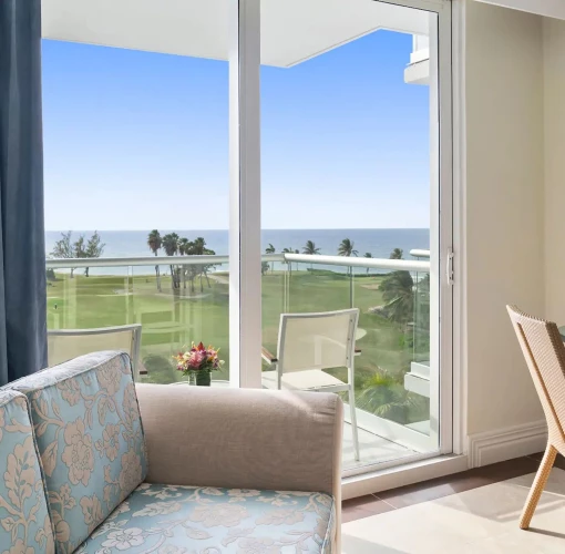 Living area of a Partial Ocean View King room with a sofa and desk, looking out onto a balcony and the ocean.