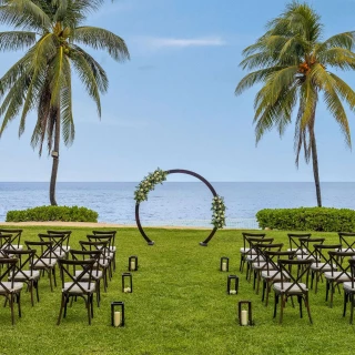 An outdoor wedding venue on the West Lawn with an arch, chairs, and lanterns set up with the ocean as the backdrop.