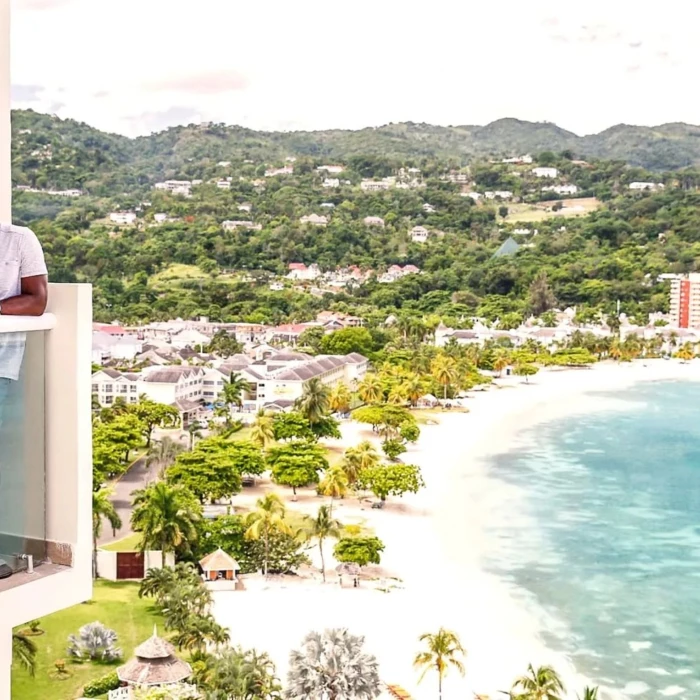 couple standing in the balcony of their suite that overlooks the sea and mountains at Moon Palace Jamaica