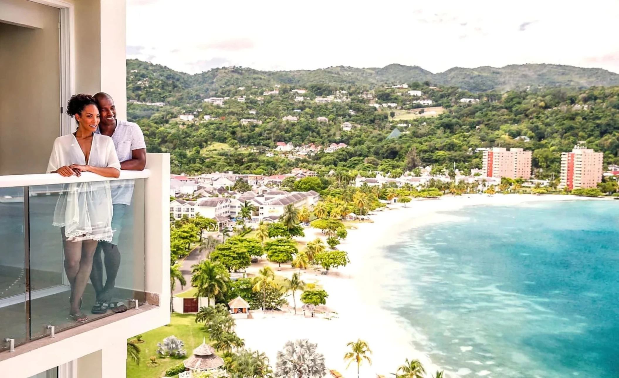 couple standing in the balcony of their suite that overlooks the sea and mountains at Moon Palace Jamaica