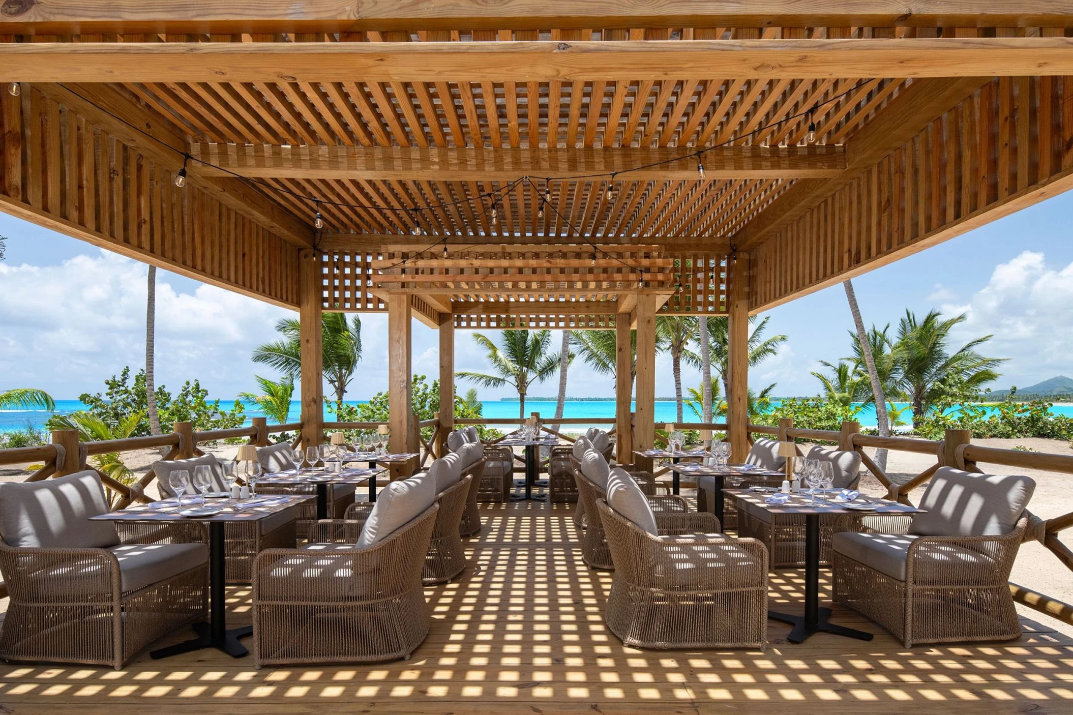 An open-air Beach Club restaurant with tables, chairs, and a stunning view of the beach and ocean.
