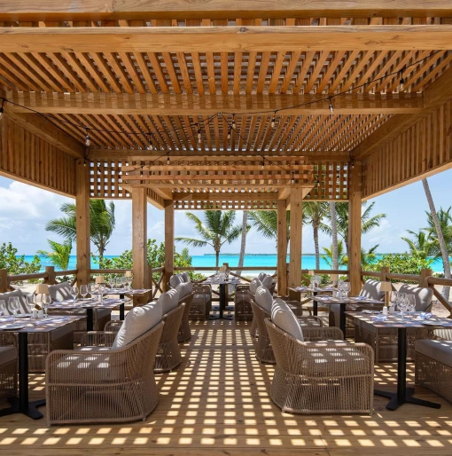 An open-air Beach Club restaurant with tables, chairs, and a stunning view of the beach and ocean.