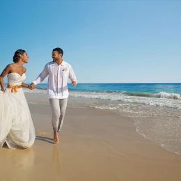 A joyful bride and groom, in wedding attire, holding hands and running along the beautiful sandy beach.