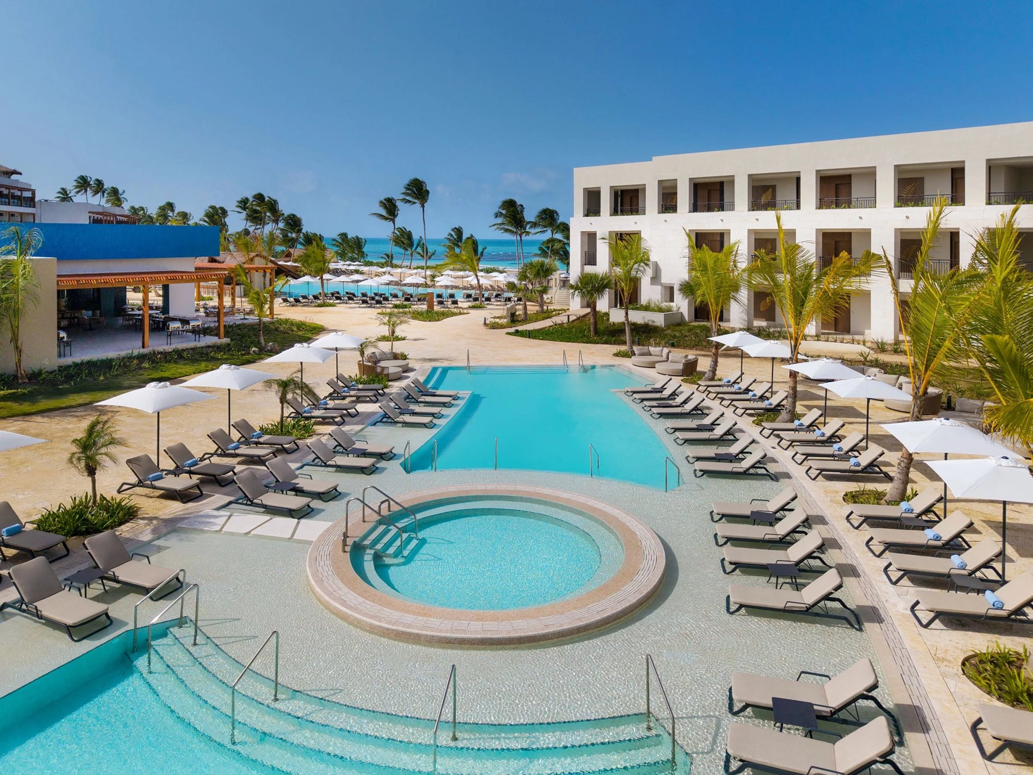 An aerial view of the large freeform pool, hot tub, and numerous lounge chairs on the resort beach.