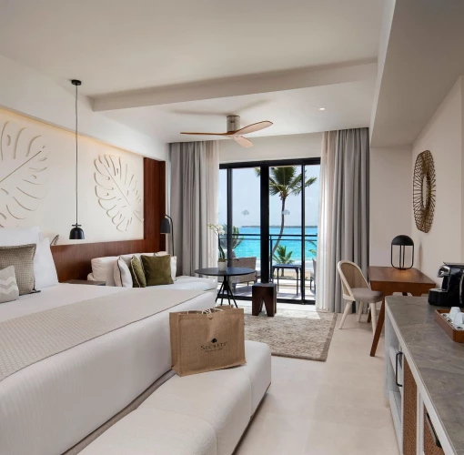 An oceanfront preferred club junior suite with a king-sized bed and balcony with a stunning beach view.