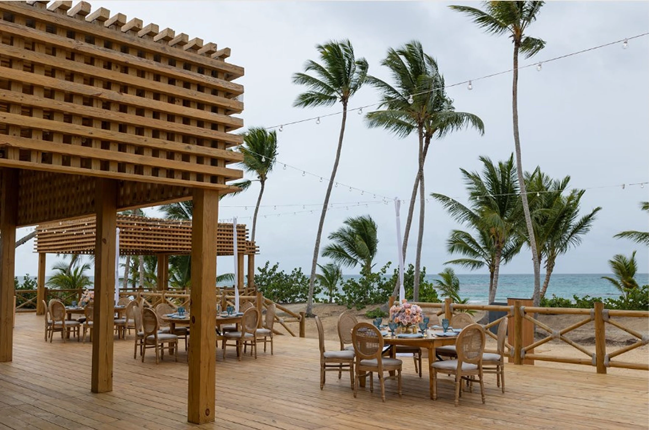 The Secrets Beach Club venue, an outdoor deck with wooden tables, string lights, and an ocean view.