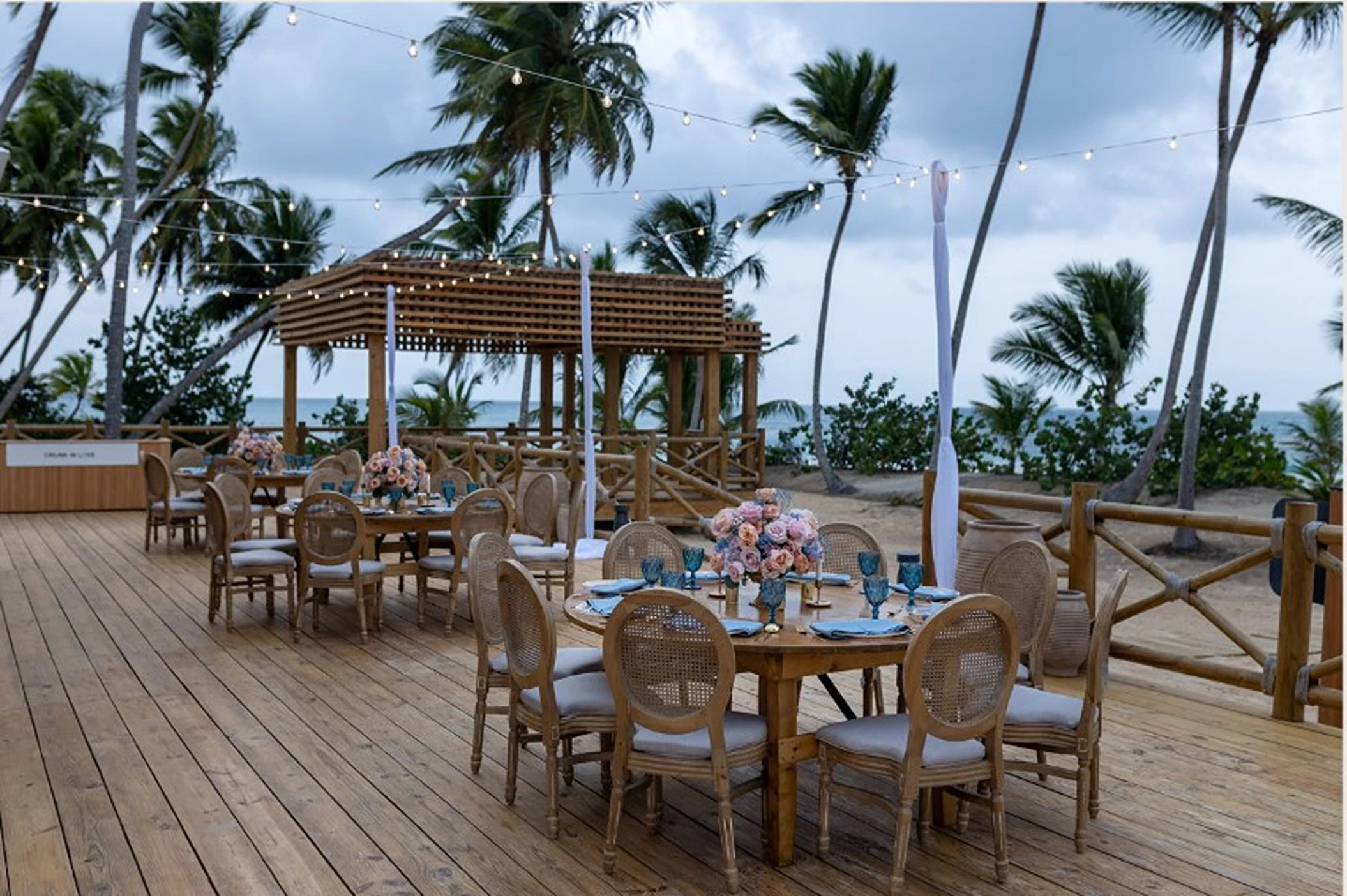A wedding venue at the Secrets Beach Club with tables set with flowers on a wooden deck by the ocean.