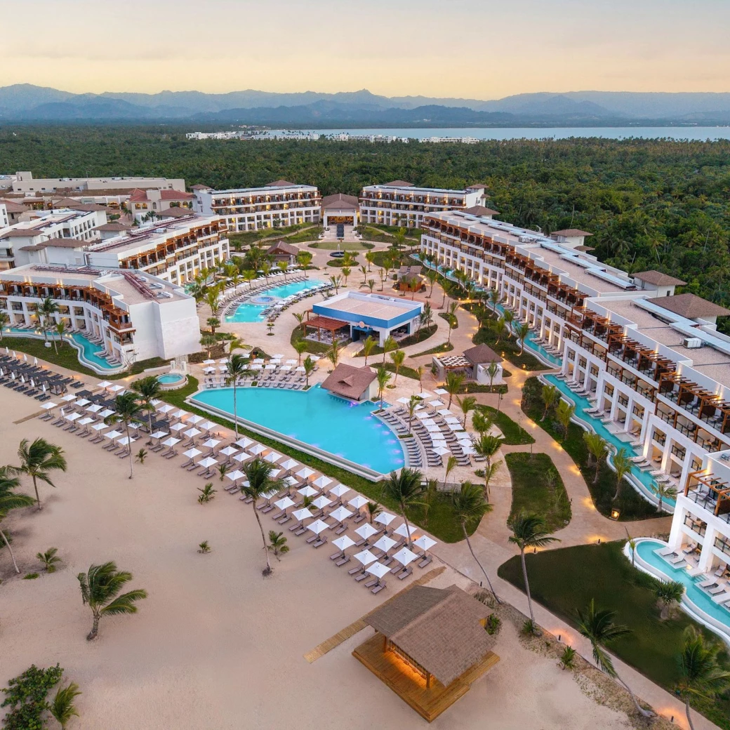 An aerial view of the Secrets Playa Esmeralda resort at sunset, with pools, beach, and lush trees.