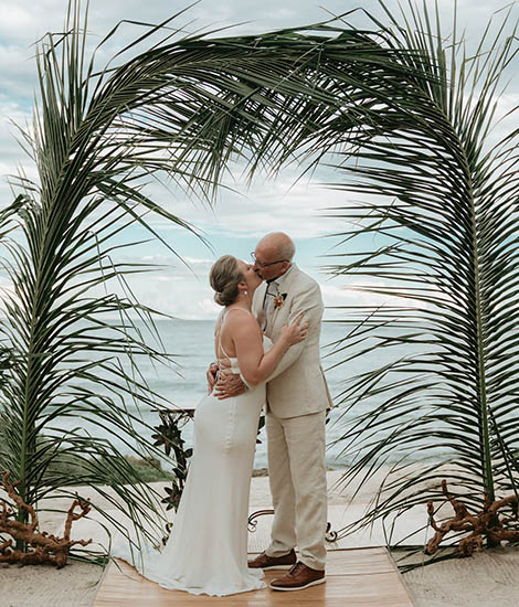 Gorm and bride's first kiss underneath a beatiful palmtree made arch